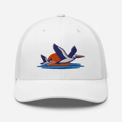 Pelicans Over Coastal Sun Trucker Cap in white with embroidered pelicans flying over a sunset and ocean waves