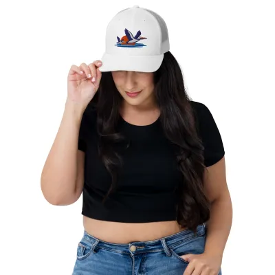 Smiling woman in a black top wearing the white Pelicans Over Coastal Sun Trucker Cap with embroidered pelicans
