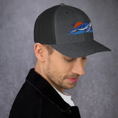 Man wearing the heather gray Cayrunner Sunset Turtle Trucker Cap with an embroidered sea turtle and sunset logo