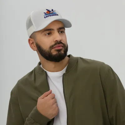 Man in a green jacket wearing the silver gray Cayrunner Pelicans Over Coastal Sun Trucker Cap with embroidered pelicans