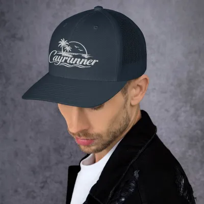 Man wearing the navy Cayrunner Logo Trucker Cap with a white embroidered palm tree, sunset, and seabird design