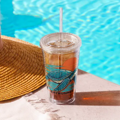 Cayrunner Sunset Turtle Clear Plastic Tumbler with an iced drink beside a pool and a straw hat