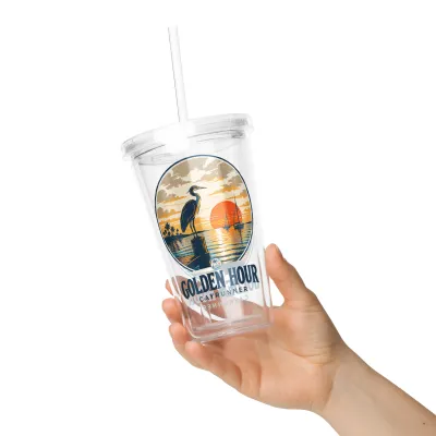 Hand holding Golden Hour Cayrunner Coastal Clear Plastic Tumbler with a heron and sunset design