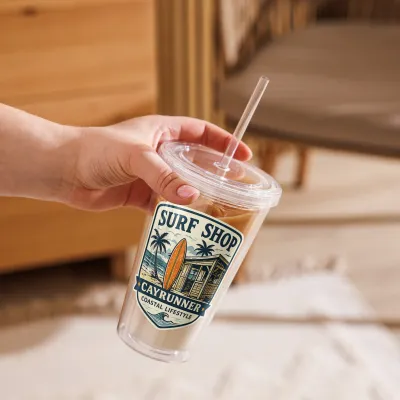 Hand holding Cayrunner Surf Shop Badge Clear Plastic Tumbler filled with iced coffee