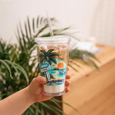 Hand holding Cayrunner Tropical Sandbar Sunset Clear Plastic Tumbler filled with iced coffee
