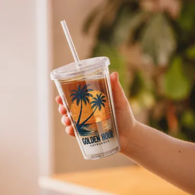 Hand holding Cayrunner Golden Hour Tropical Sunset Clear Plastic Tumbler filled with iced coffee