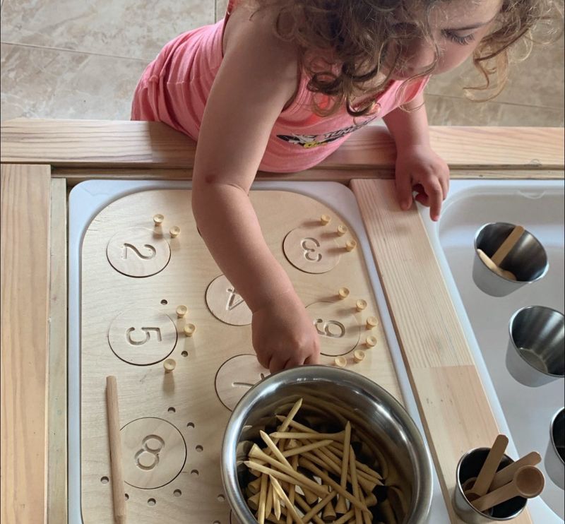 Παιδί παίζει με πίνακα αριθμών Montessori, μαθαίνοντας χρώματα, ποσότητες και αριθμούς μέσα από αισθητηριακό παιχνίδι.