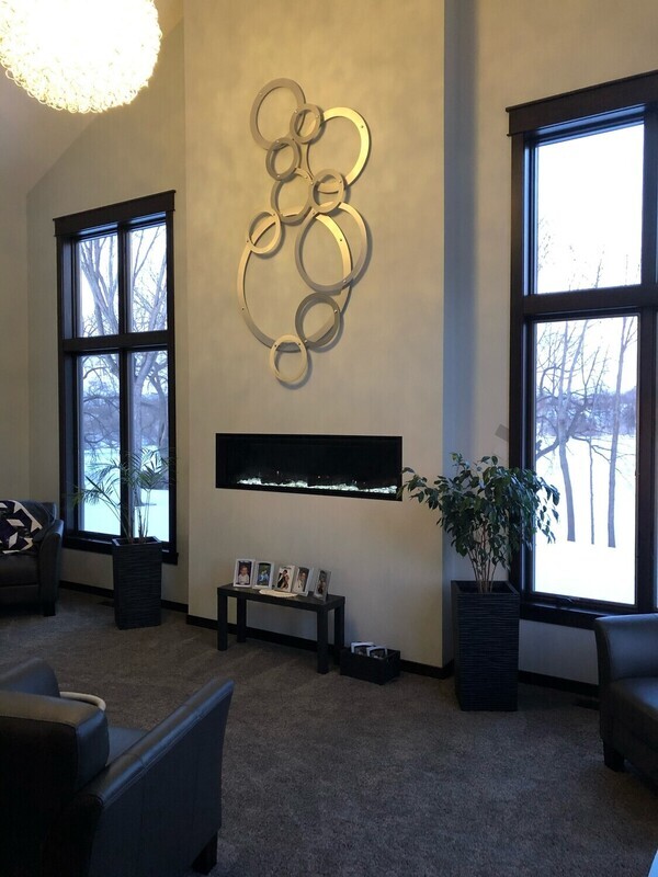 A modern living room with high ceilings showcases a custom metal sculpture mounted above a long, nar...