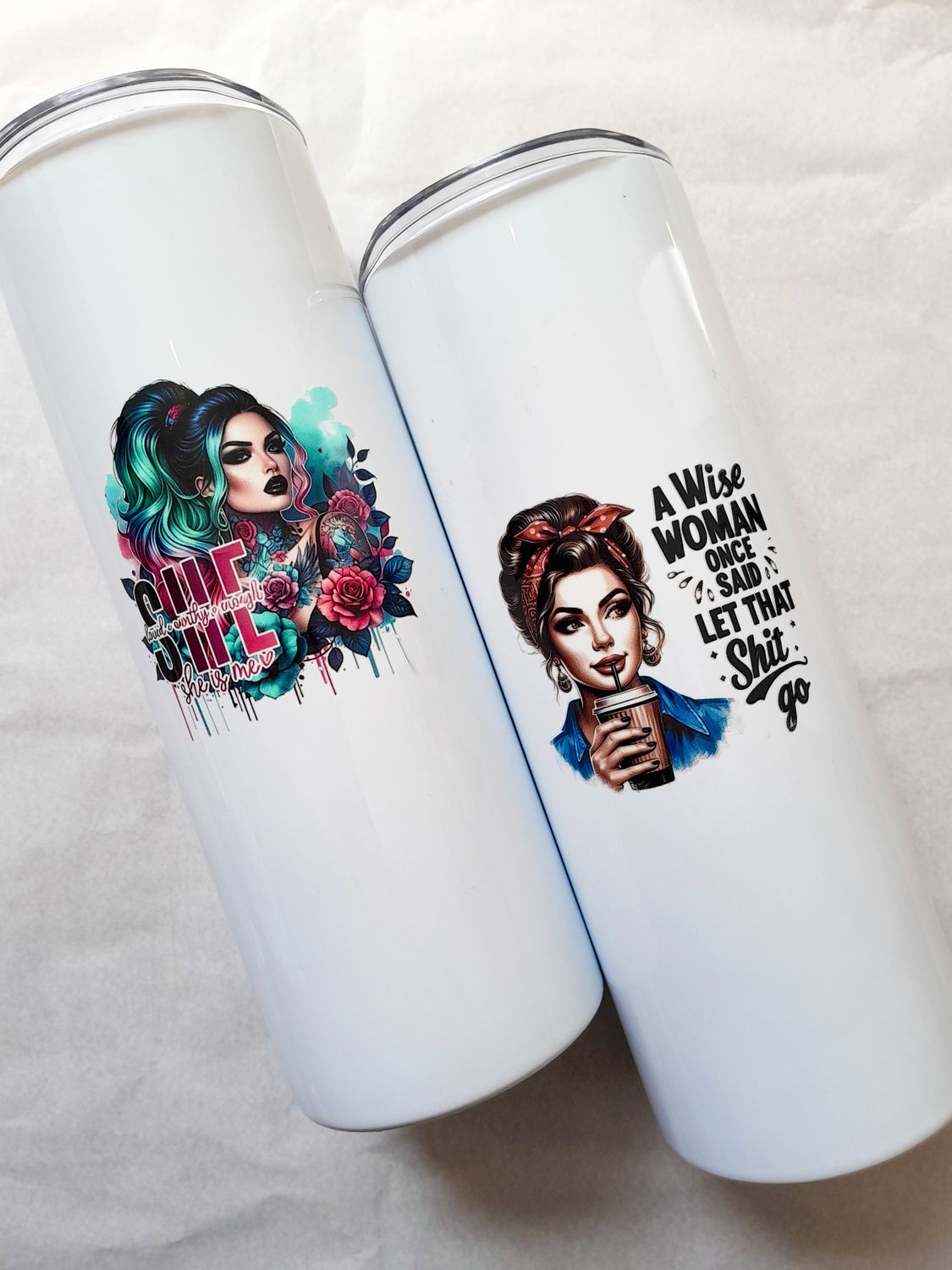 Two white skinny tumblers side by side with women empowerment designs, each with an included glass straw.