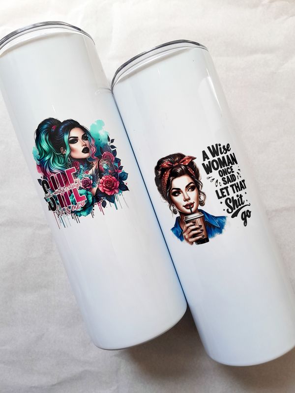 Two white skinny tumblers side by side with women empowerment designs, each with an included glass straw.