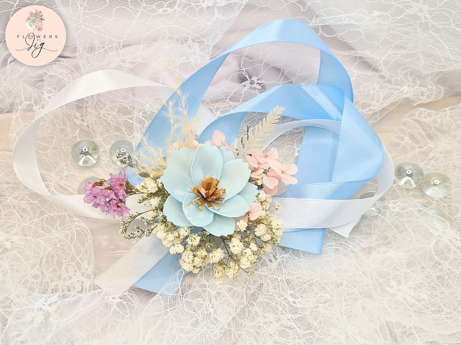Add sophistication to your events with this handcrafted Baby Blue Cosmos corsage/boutonniere set. Made from sola wood and accented with gypsophila, fern, statice, hydrangea, and sky blue and white ribbons, ideal for weddings and proms.