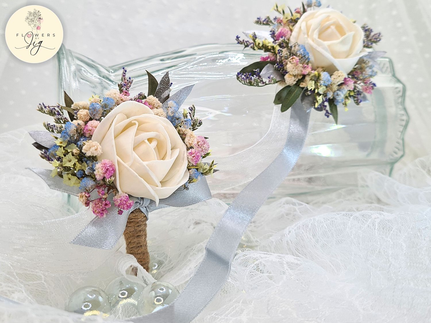 Handcrafted white sola wood corsage with blue and pink dried flowers, eco-friendly, perfect for weddings and proms, featuring a silver satin ribbon. Realistic and long-lasting floral accessory.