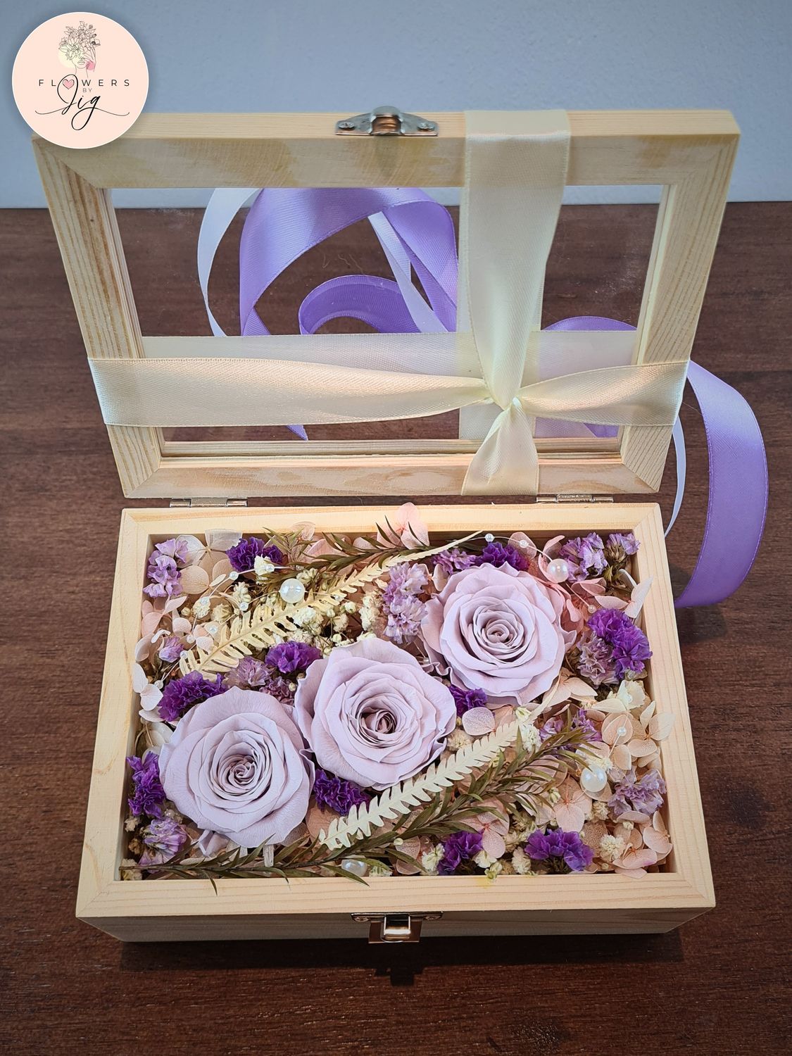 Experience timeless beauty with our Pinewood Box featuring 3 Vintage Purple Infinity Roses and assorted dried flowers. Perfect for gifts, this bouquet includes ferns, gypsophila, and decorative pearls, all encased in a glass-covered box.