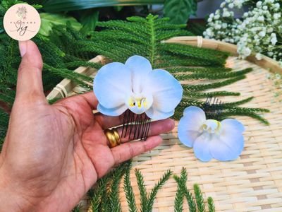 Handmade light blue tropical orchid hairpin in polymer clay with a detailed gradient from light blue to a sharp yellow center. Realistic, lightweight, durable bridal accessory perfect for weddings, tropical events, vacations, and formal occasions