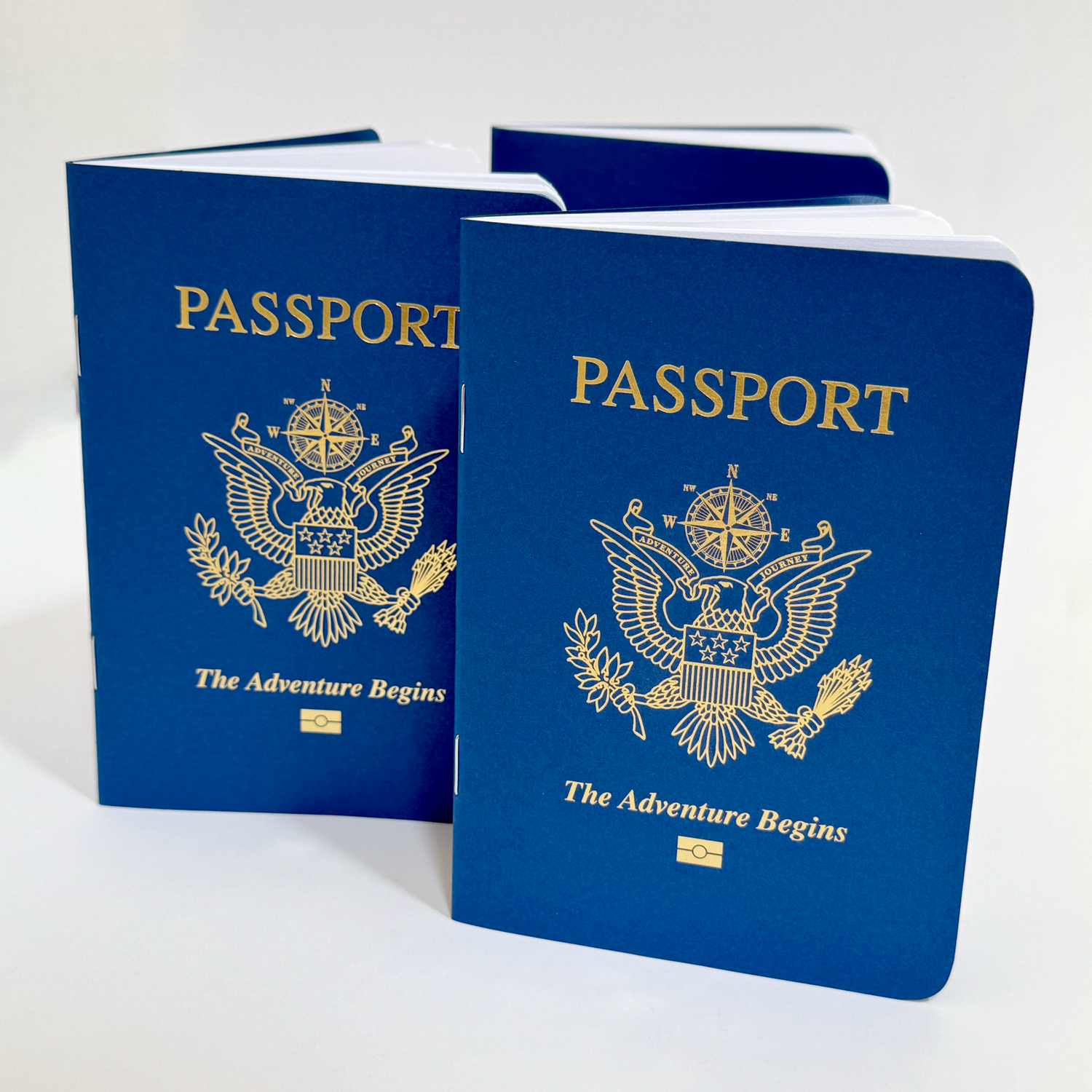 Mini notebooks that resemble a United States of America passport that have a blue card stock cover with the word "Passport" at the top, a modified eagle emblem in the middle, and the words "The Adventure Begins" below. The design on the cover is printed with shiny gold foil, and there are 12 blank white pages inside the 3.5" x 5" size notebook.