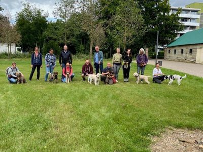 Seminargruppe mit Hunden auf einer Wiese bei Sonnenschein nach erfolgreichen Übungen zur Trüffelsuche.