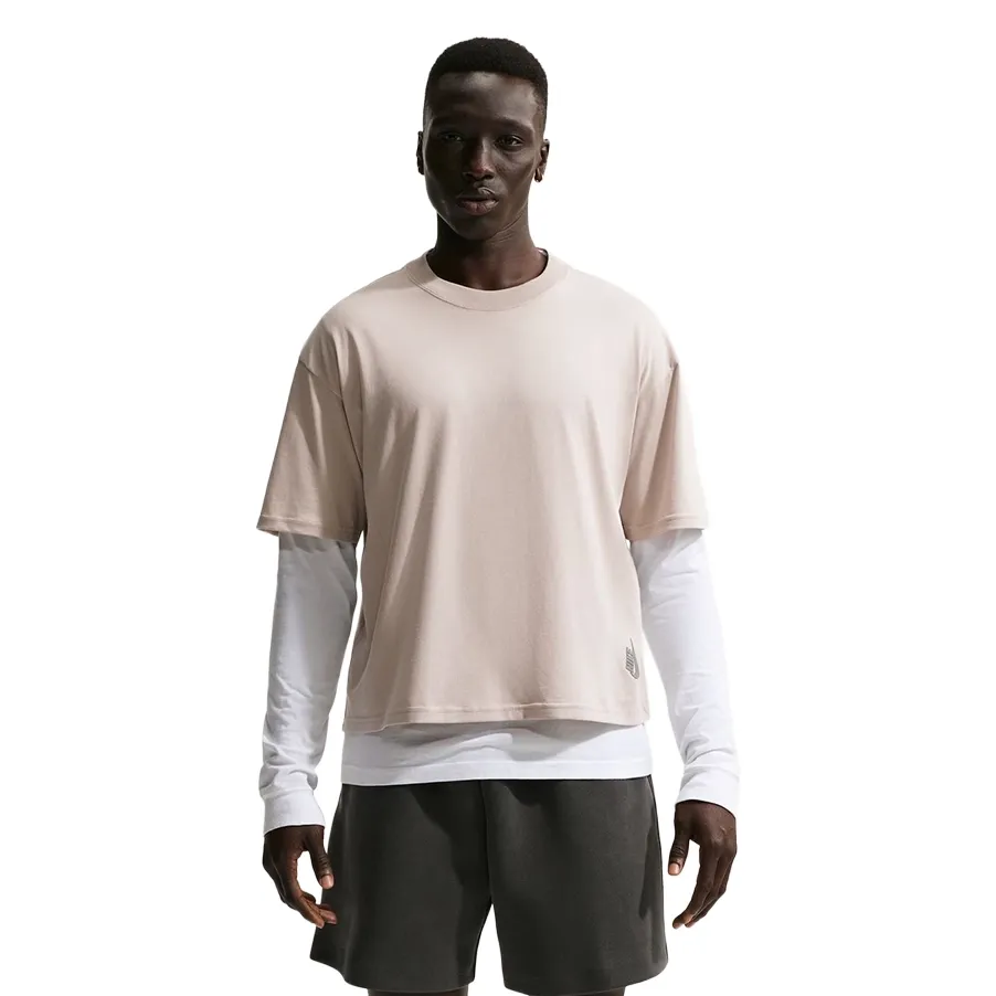 Front view of cream boxy Nike tee layered over white long-sleeve, worn with dark shorts