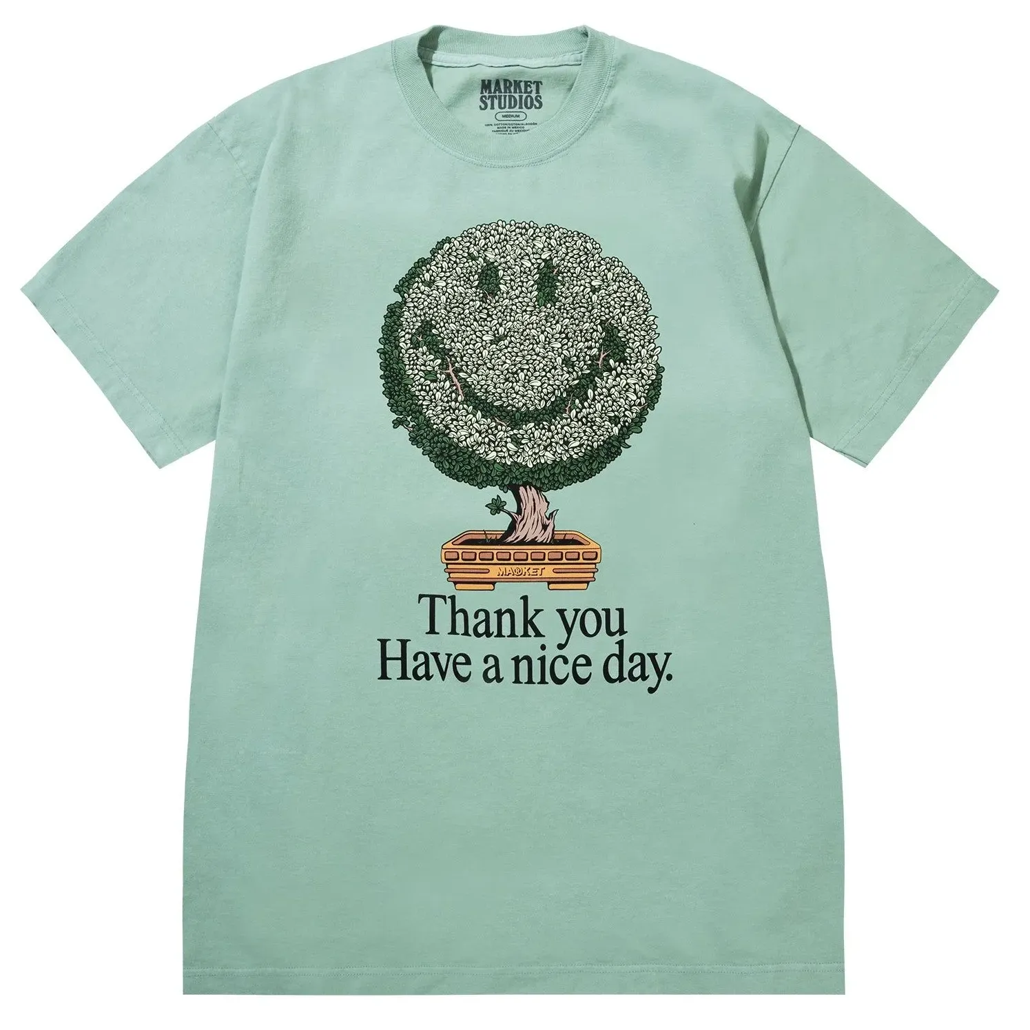 Front view of Market Studios green t-shirt with smiley bonsai tree graphic and “Thank you Have a nice day” text