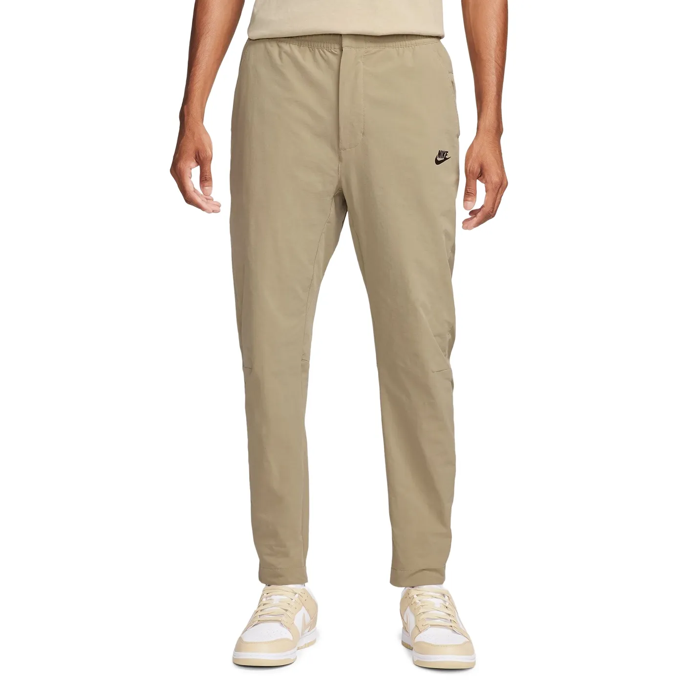 Front view of Nike Commuter woven pants in khaki with tapered legs, open hems and black Nike logo.