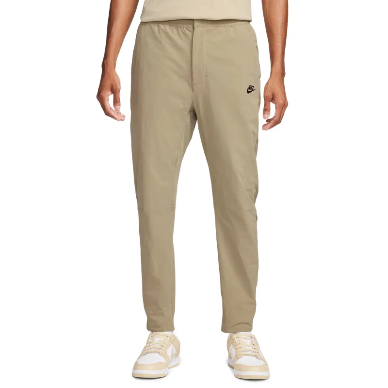 Front view of Nike Commuter woven pants in khaki with tapered legs, open hems and black Nike logo.