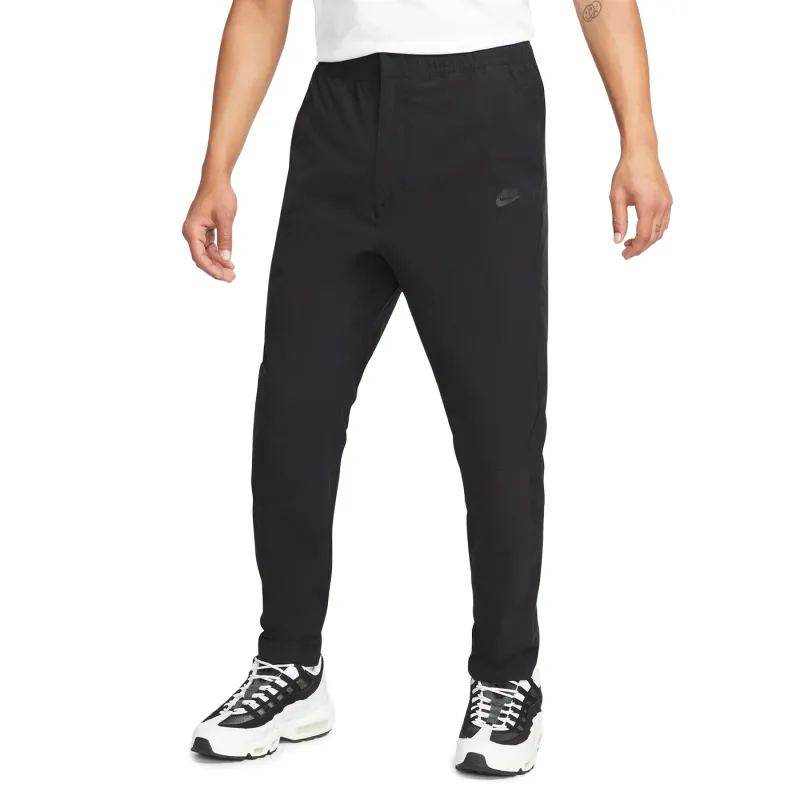 Front view of black Nike Commuter woven pants with tapered legs, open hems and tonal Nike branding.