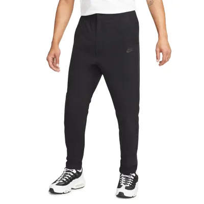 Front view of black Nike Commuter woven pants with tapered legs, open hems and tonal Nike branding.