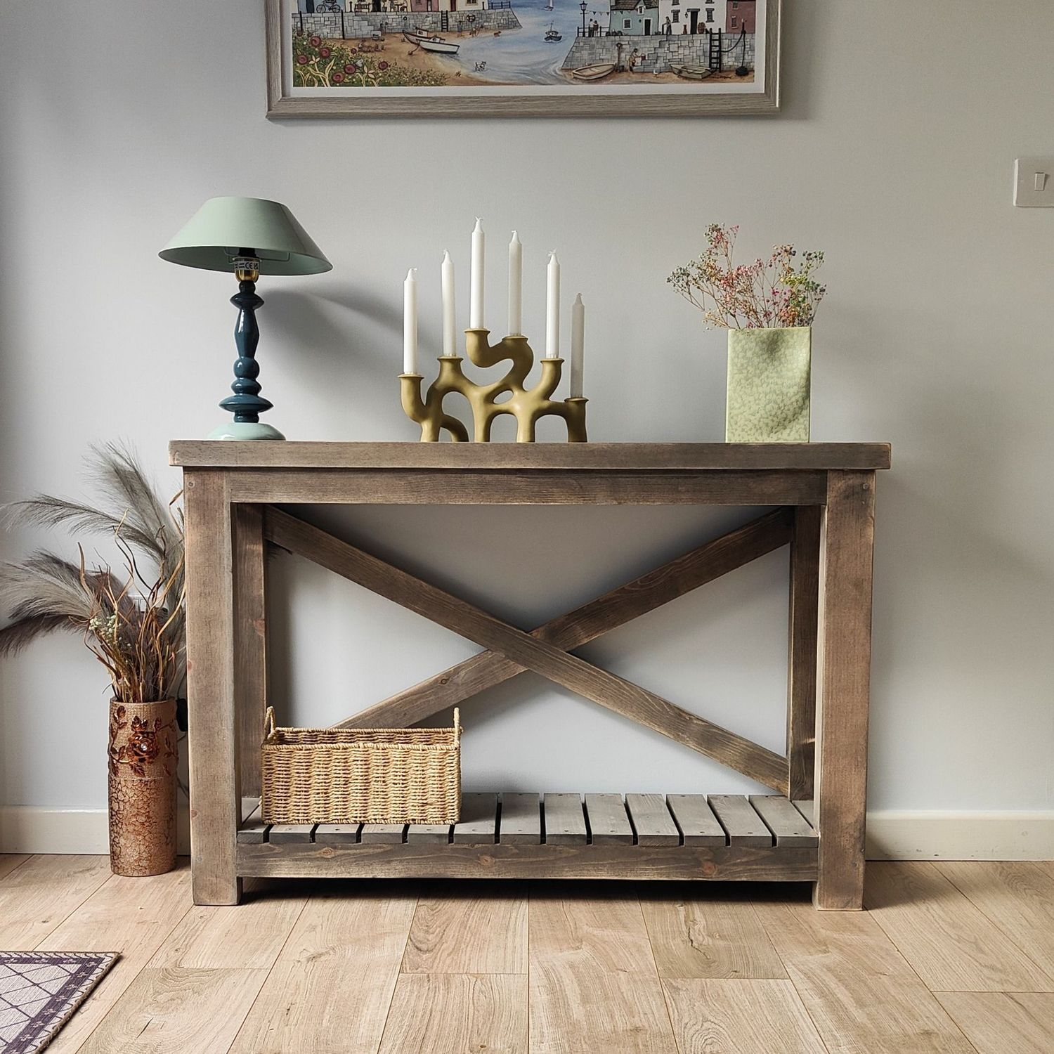 A rustic wooden console table with a dark-stained finish, featuring a sturdy farmhouse-style design. The table has thick legs, a slatted lower shelf, and a distinctive X-shaped support on the back.