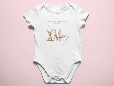 A soft white personalised baby grow featuring a whimsical rabbit illustration and “Our First Mother’s Day” text, designed as a sentimental keepsake for mums.