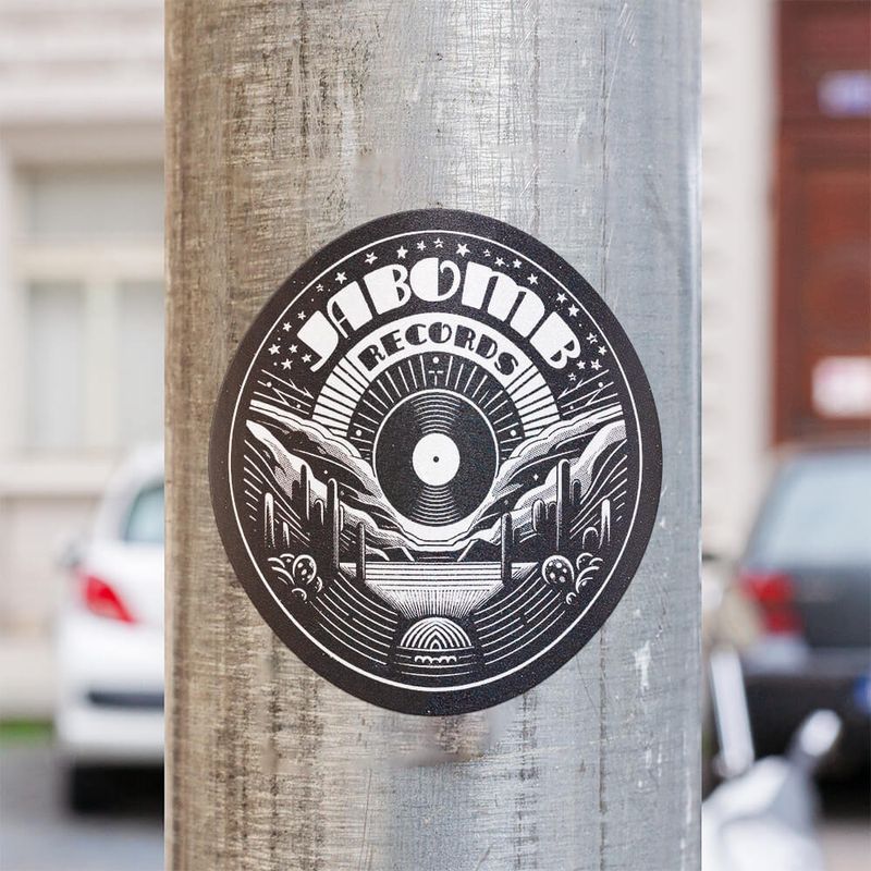 Jabomb Records logo on a round sticker placed on a utility pole in a city street.