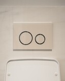 Plaque de déclenchement ronde Geberit Sigma50 avec verre gris brillant et boutons chromés encastrés.
