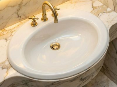 Vasque encastrable Bornéo 60 cm Vasque encastrable Bornéo 60 cm, lavabo en céramique blanche avec robinet doré et contour de comptoir en marbre.