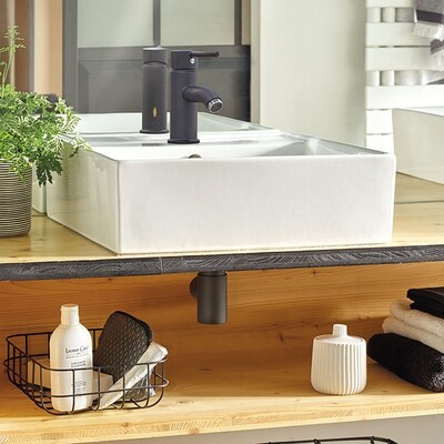 Mini siphon de lavabo Wirquin Linéis noir mat sous lavabo blanc sur étagère de salle de bain en bois.