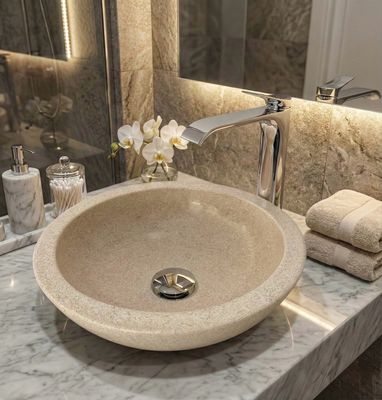 Bol à poser Bolero 44 cm granité corail Lavabo en pierre beige mouchetée avec robinet argenté sur un comptoir en marbre, serviettes et articles de toilette à proximité.
