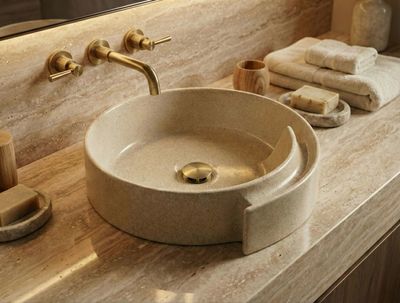 Bol à poser Arobase 40 cm granité beige Évier en granit beige avec tablette intégrée et robinet doré sur un comptoir en marbre avec serviettes.