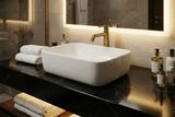 Lavabo rectangulaire en céramique blanche avec robinet doré sur un plan de travail en marbre noir, style Geberit Aniara.