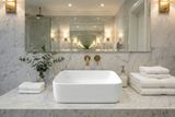 Lavabo rectangulaire en céramique blanche sur un plan de travail en marbre avec robinetterie dorée et serviettes empilées à proximité.