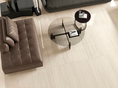 Carrelage en céramique beige au sol du salon, canapé marron et table basse en verre à proximité.