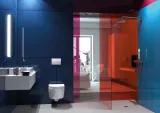Plaque de commande carrée chromée Geberit Alpha01 sur un mur de salle de bains bleu foncé avec toilettes et lavabo blancs.