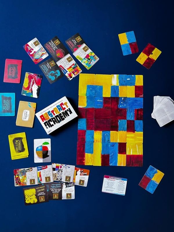 A table with the game &quot;abstract academy&quot; setup on it. A colorful board for the game and cards with art references.