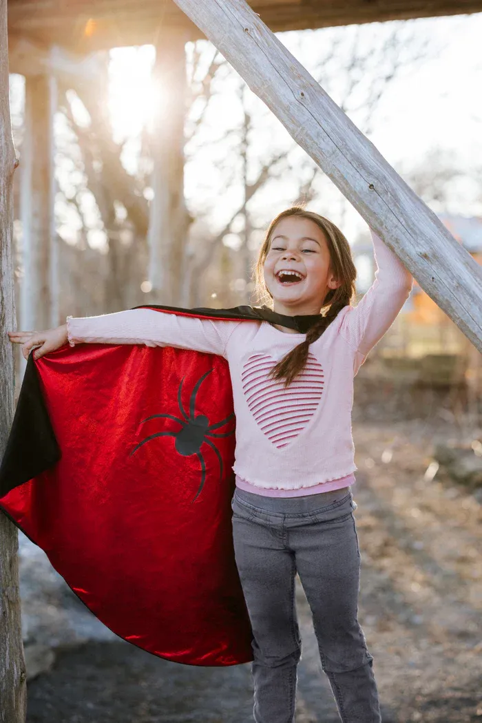 A small child excited about her new reversible hero cape.