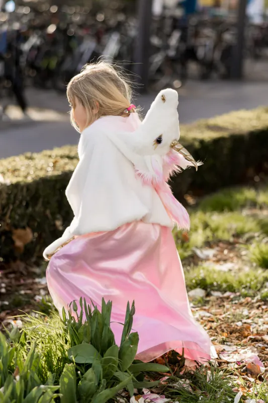 A small girl running in a white and pink unicorn cape.