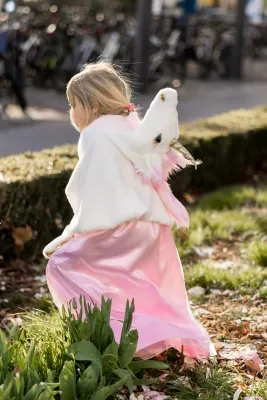 A small girl running in a white and pink unicorn cape.