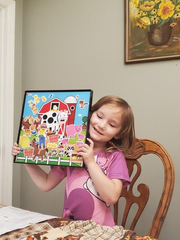 A small child holding up her colorforms farm with all of the stickers included.