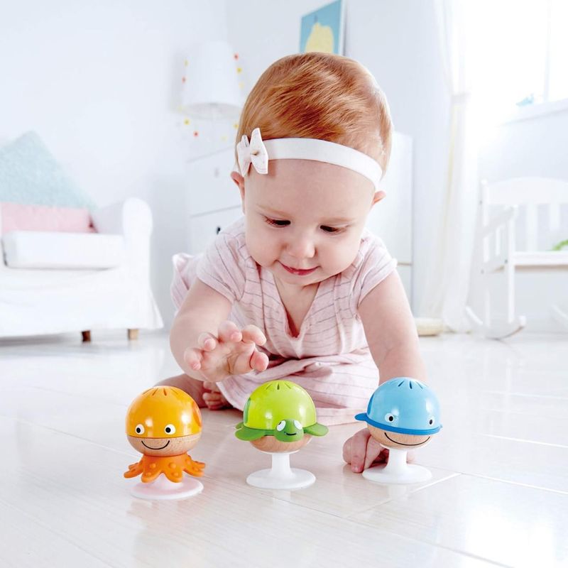 A cute baby playing with 3 suction cup shakers that have cute animal designs.