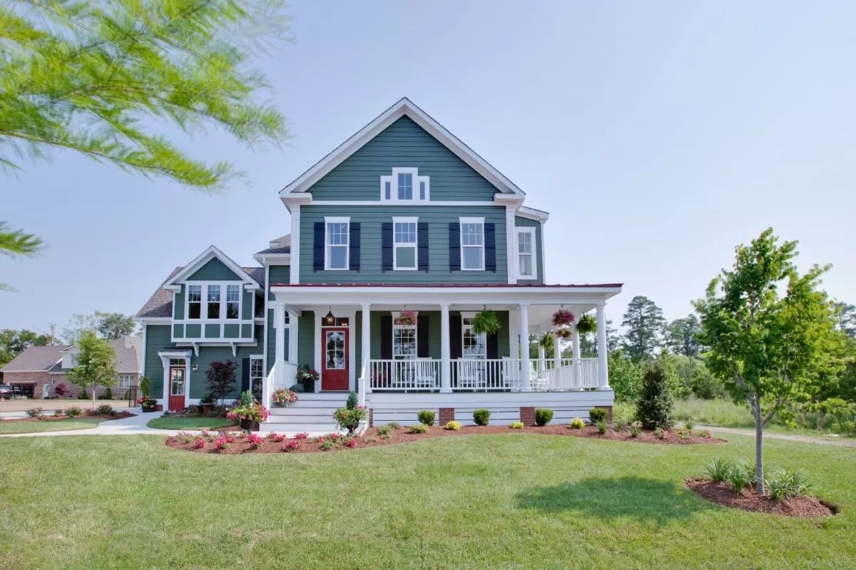 Front view of a large two story white house with gray roof, wraparound porch, manicured lawn and trees around.