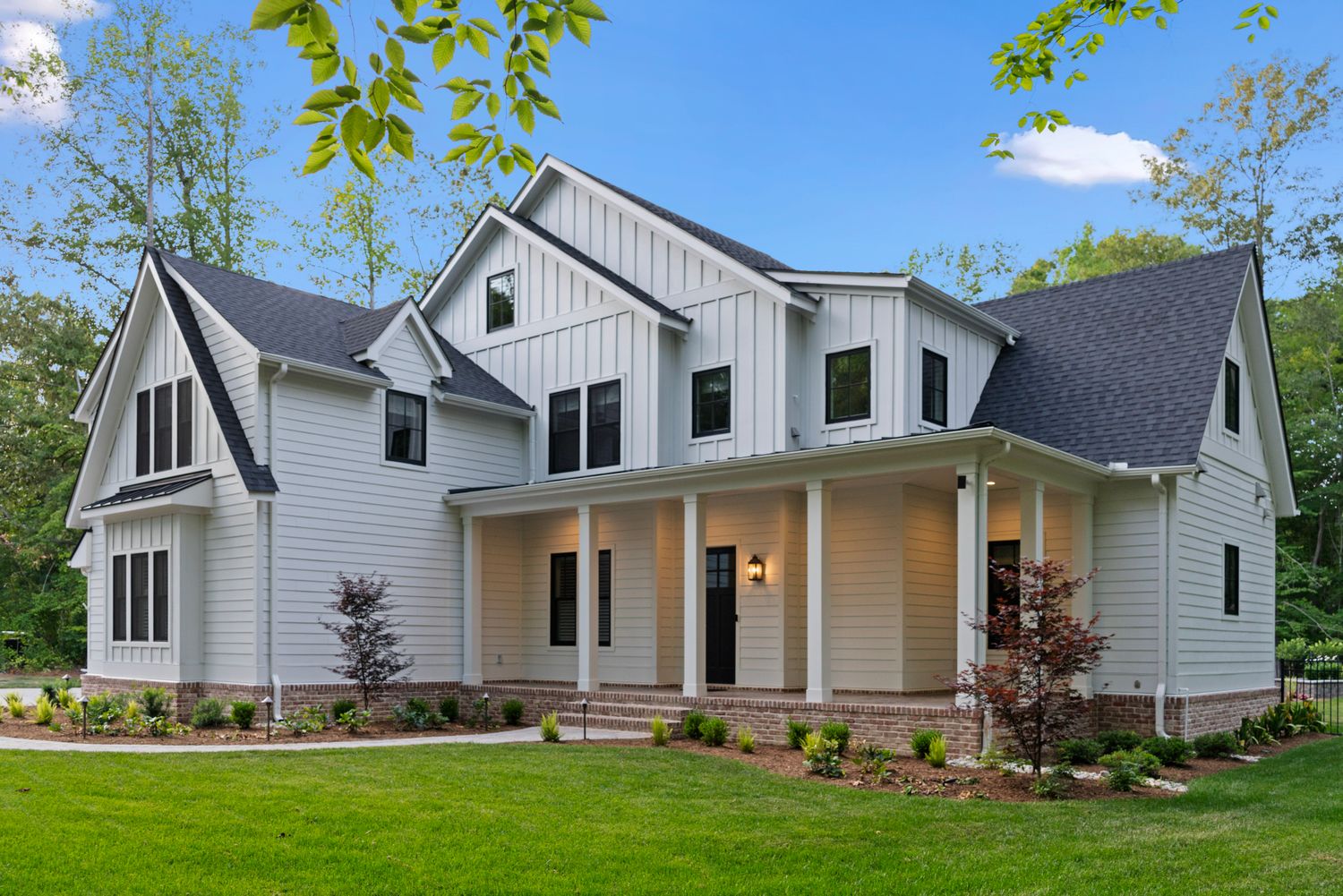 Exterior rendering of a modern farmhouse-inspired home plan with white board-and-batten siding, covered wraparound porch.