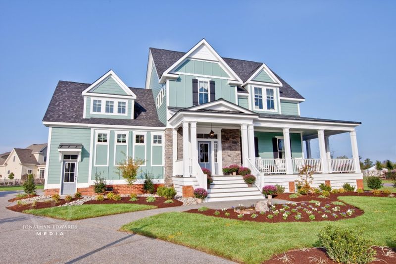 Front view of a coastal style two story house with gray siding, white porch railings, steps and flower beds.
