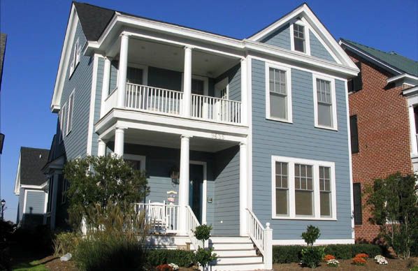 Front exterior of a two-story blue house with white trim, covered porch, balcony railing, and landscaped yard.