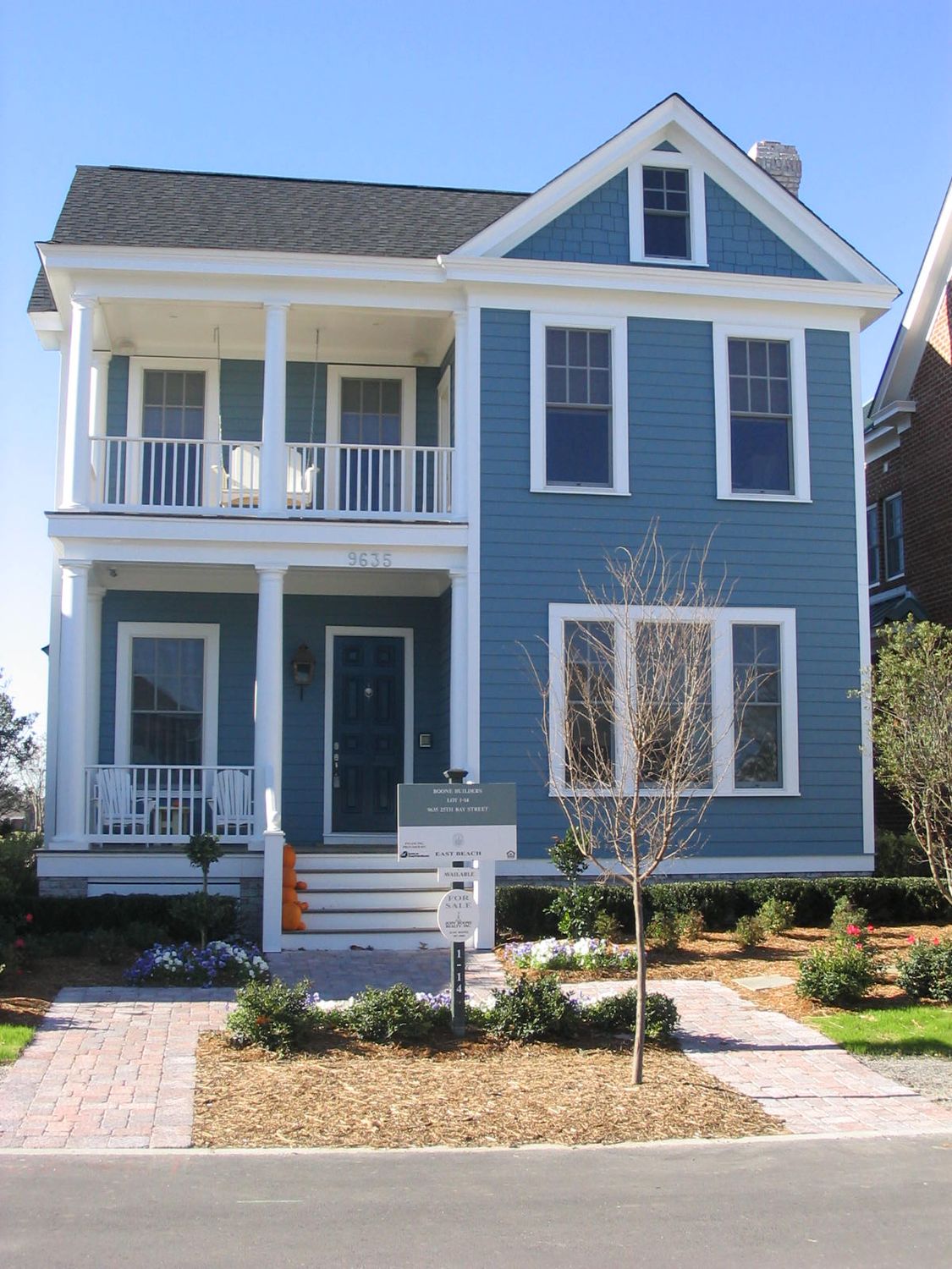 Front exterior of a two-story blue house with white trim, covered porch, balcony railing, and landscaped yard.