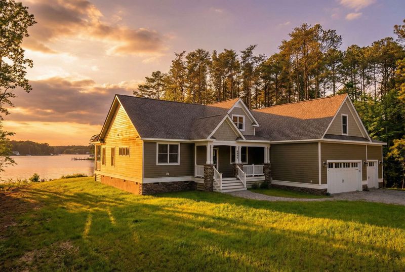 Front view of beige single-story house with gable roof, two-car garage, driveway, and trees around lawn area.